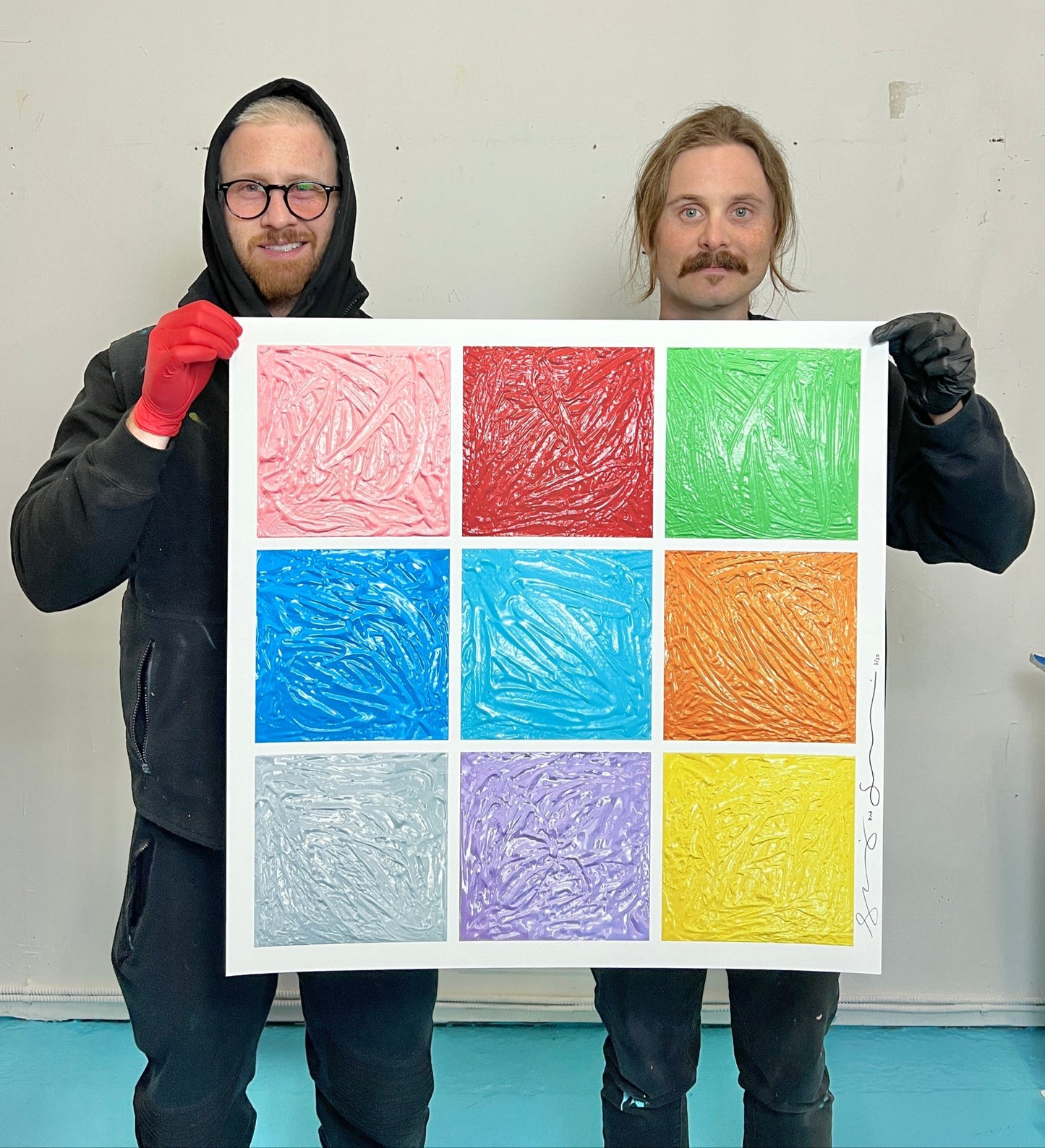 Two people holding a square with six colored squares of different textures against a plain background