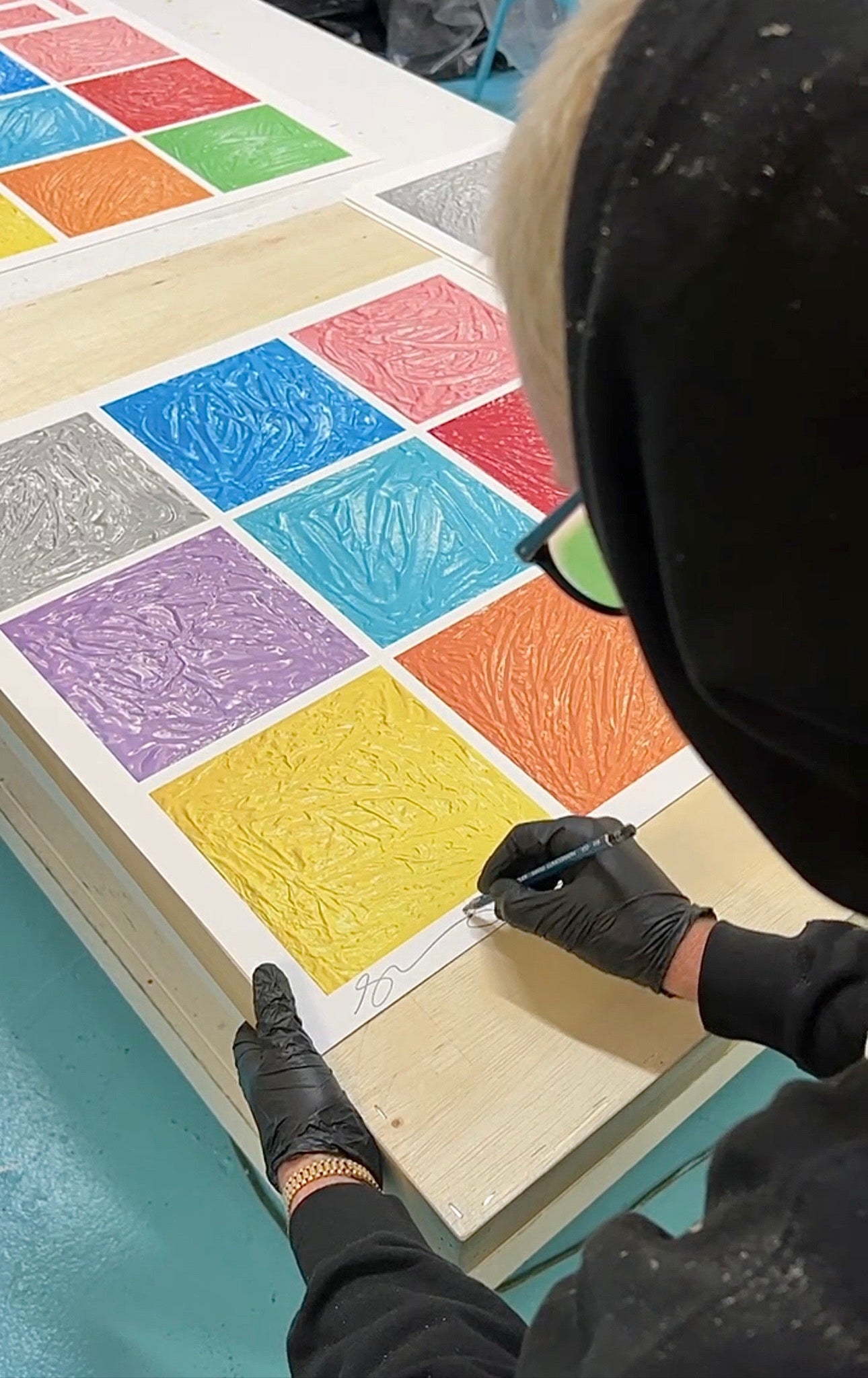 Person working on a colorful art project with textured squares on a table.