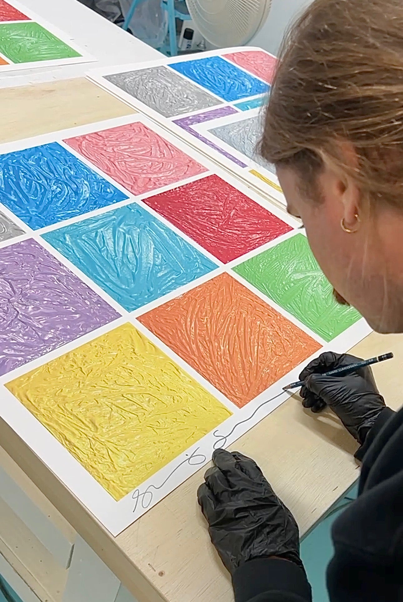 Person wearing black gloves working on a colorful textured art project.