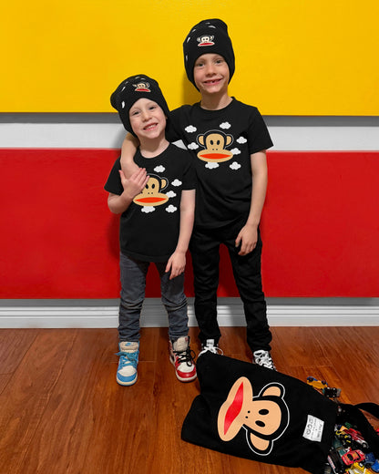 Two children wearing matching black t-shirts with a cartoon monkey design in front of a colorful wall.