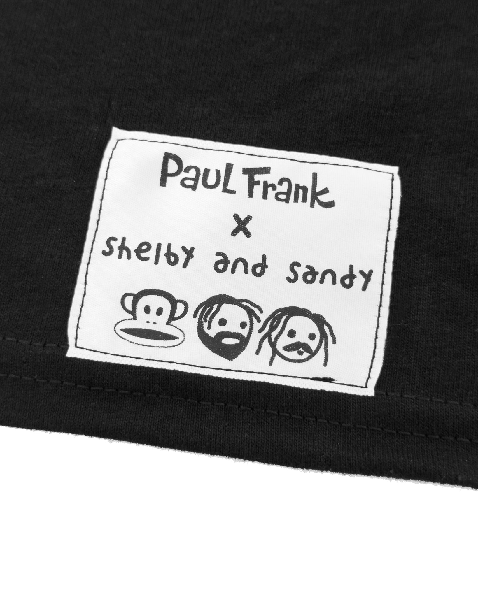 Close-up of a label on a black garment featuring 'Paul Frank x Shelby and Sandy' design.